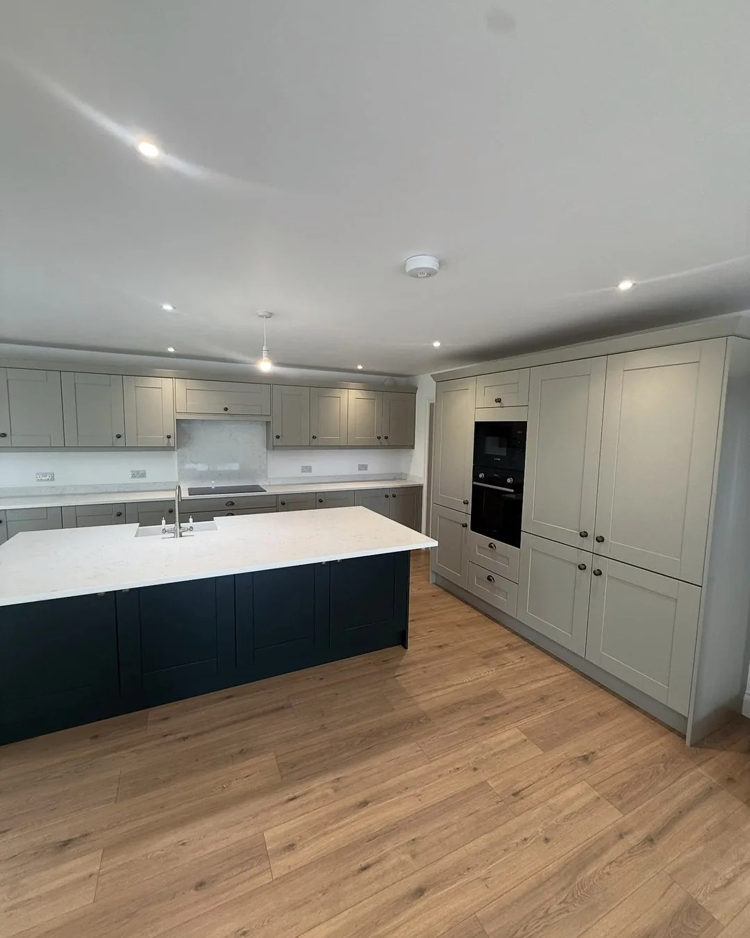 New-build kitchen with island, oven bank and recessed ceiling lighting