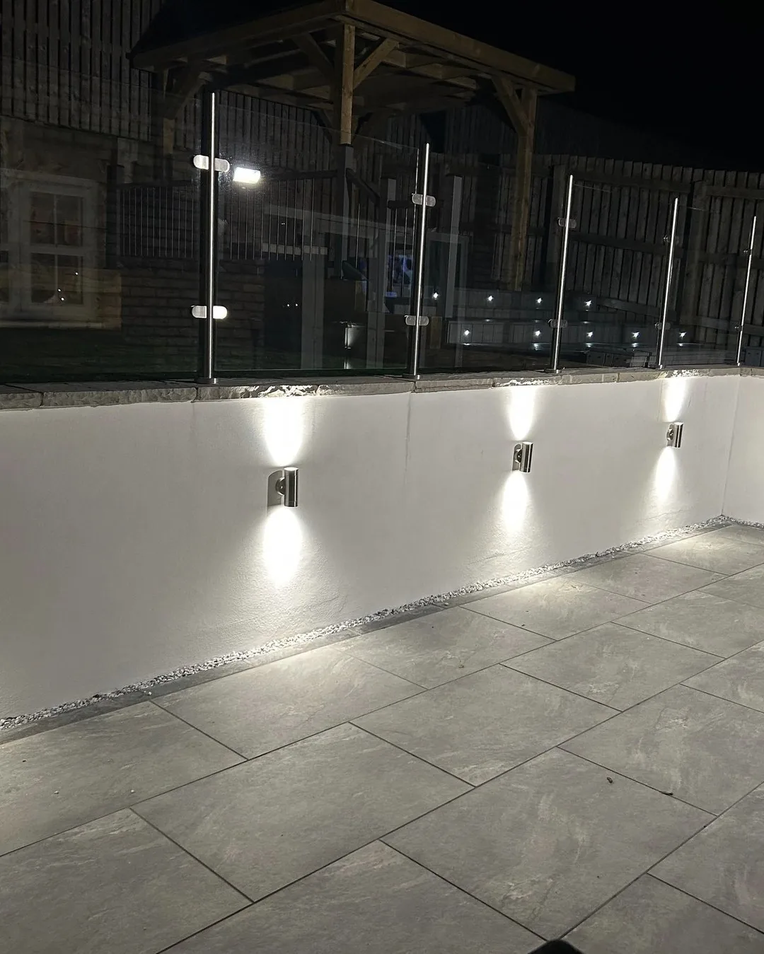 Outdoor wall lights illuminating a finished garden patio and glass balustrade