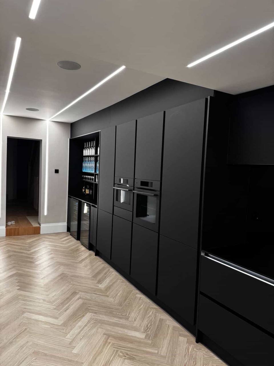 Finished matte-black kitchen with linear ceiling lighting and herringbone floor