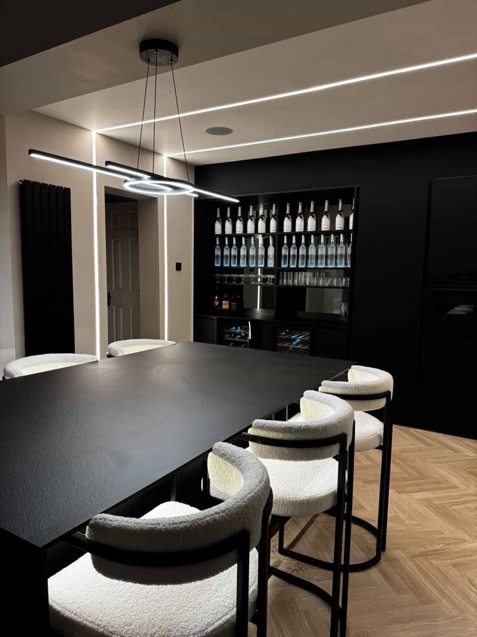 Large kitchen island with pendant light, dining chairs and illuminated drinks shelving